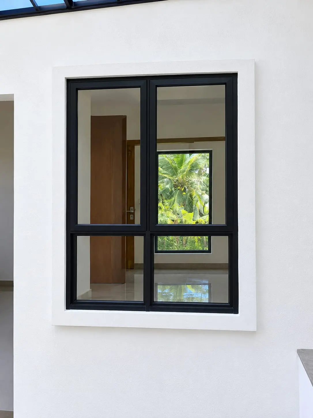 Black aluminium four-pane window set in a white wall, palm trees seen through it
